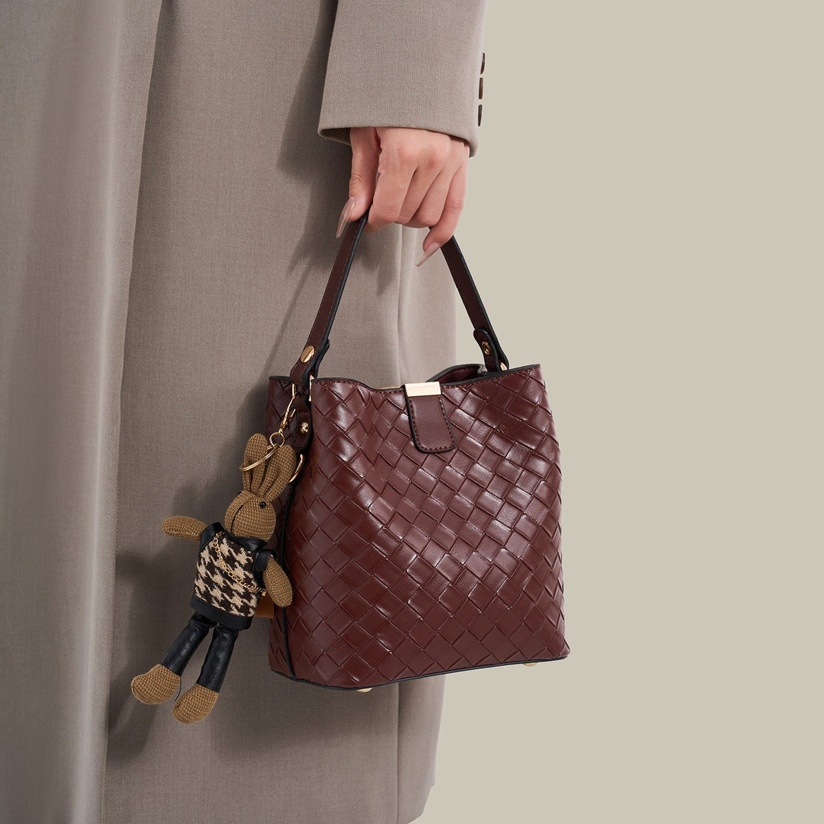 Brown woven-emboss leather-look bucket bag with short top handle, detachable crossbody strap, gold-tone hardware, and rabbit