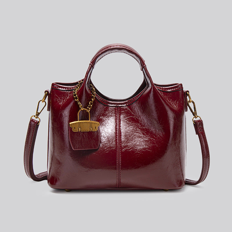 Structured crinkle-gloss top-handle satchel in deep burgundy with antique gold lock charm and detachable shoulder strap