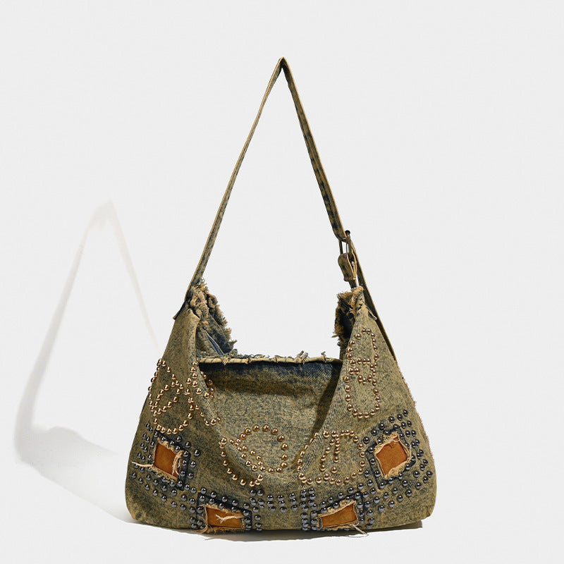 Large distressed denim hobo shoulder bag with mixed-metal rivet detailing and tan leather-look corner trim, front view