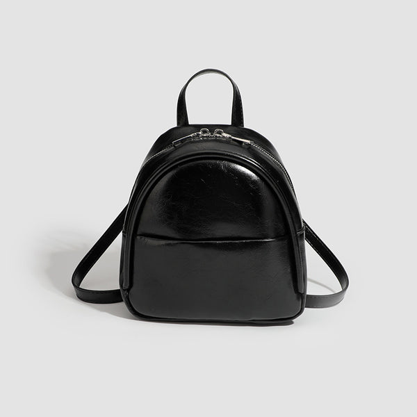 Kompakter, abgerundeter Mini-Rucksack im Lederlook mit glänzender Oberfläche, Reißverschluss oben, Vordertasche und Tragegriff oben, Vorderansicht