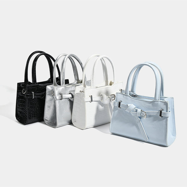Small structured trapezoid mini top-handle bag with front belt-knot buckle detail and glossy leather-look finish, detail view