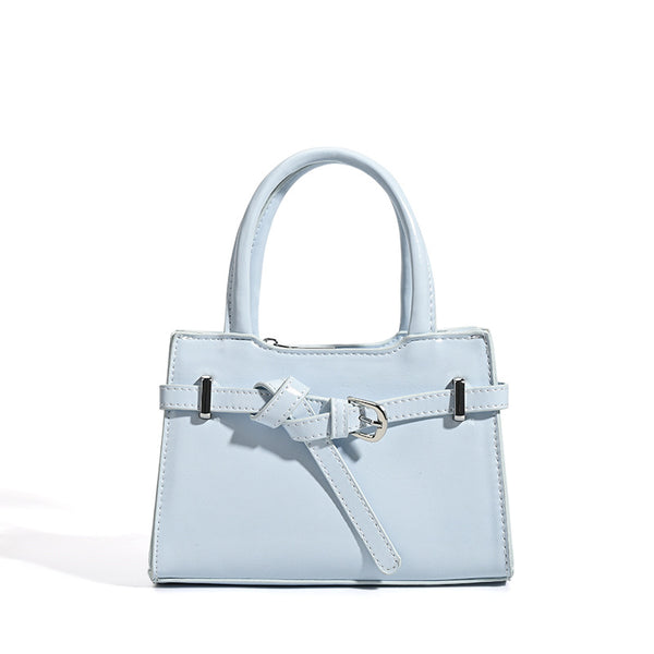 Small structured trapezoid mini top-handle bag with front belt-knot buckle detail and glossy leather-look finish, detail view