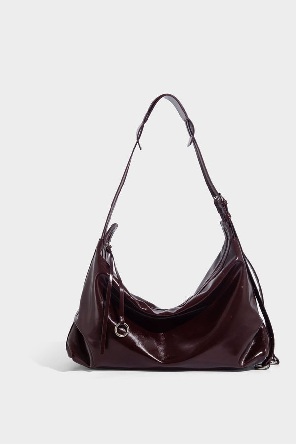 Glossy black slouchy hobo shoulder bag with zip closure, silver-tone ring hardware, and adjustable crossbody strap, detail