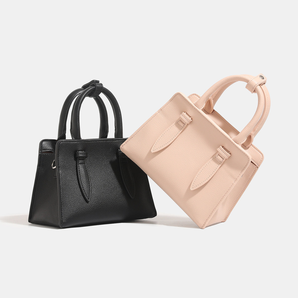 Small structured trapezoid top-handle bag in pebbled matte finish with decorative strap tabs, twin knotted handles, and