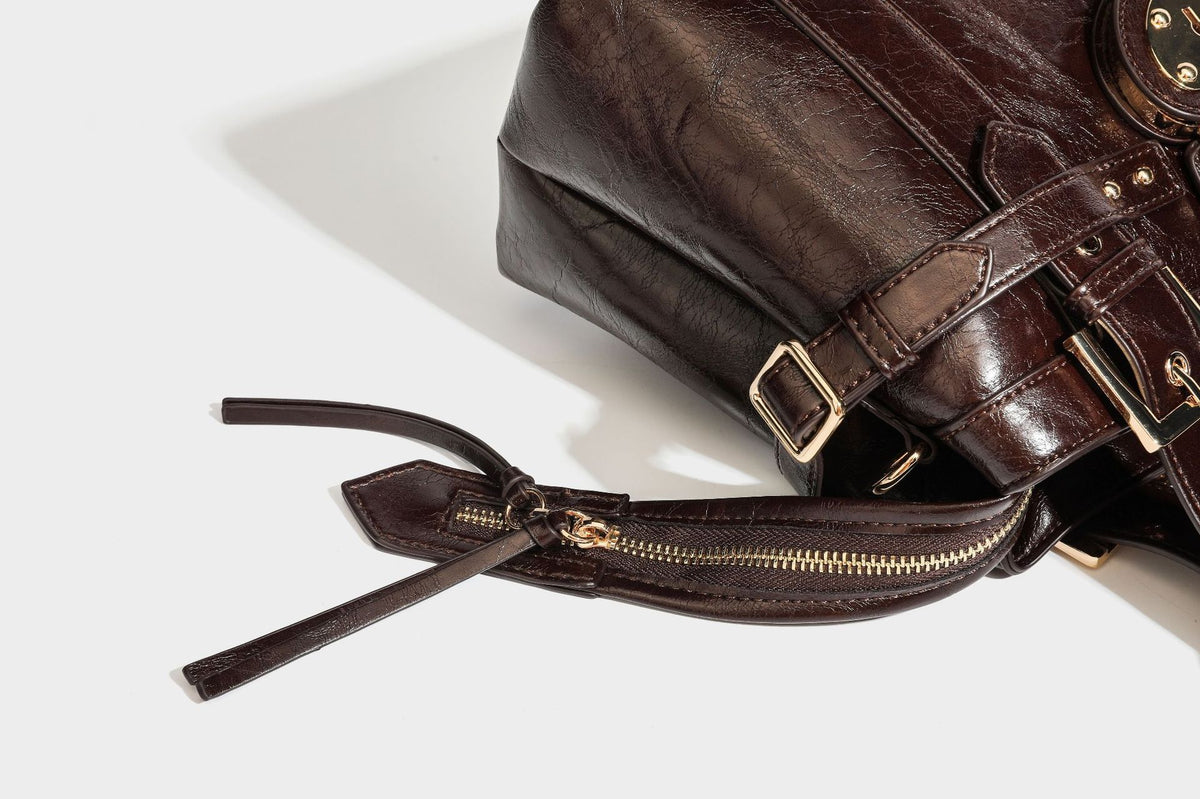 Structured leather-look satchel bag with heart padlock charm, star charm, gold-tone buckle hardware, dual top handles, and