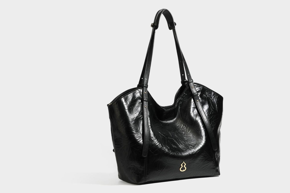 Große, glänzende Tote-Bag aus schwarzem Lederimitat mit geknitterter Optik, lässig fallender Trapezsilhouette, zwei Schulterriemen und goldfarbenen