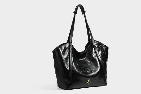 Große, glänzende Tote-Bag aus schwarzem Lederimitat mit geknitterter Optik, lässig fallender Trapezsilhouette, zwei Schulterriemen und goldfarbenen