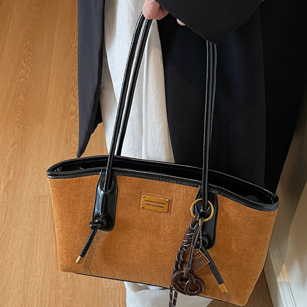 Structured suede-finish tote bag with glossy black leather-look trim, dual top handles, and decorative hanging charm in