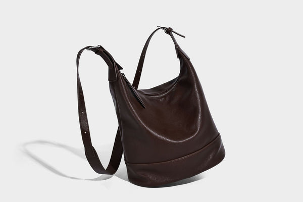 Slouchy bucket hobo shoulder bag in dark brown with glossy leather-look finish, top zip closure, and long adjustable, detail