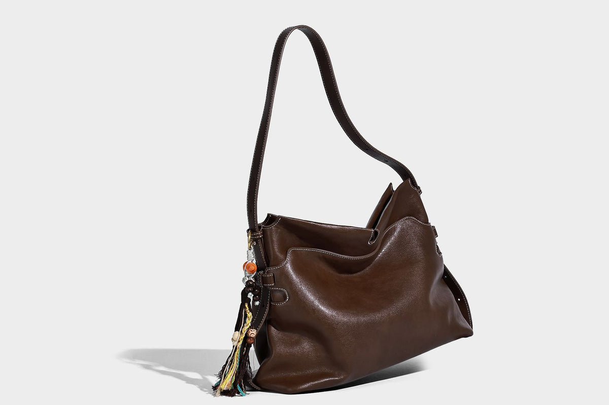Large slouchy leather-look hobo tote bag with open top, adjustable shoulder strap, and colorful tassel bead charm, detail
