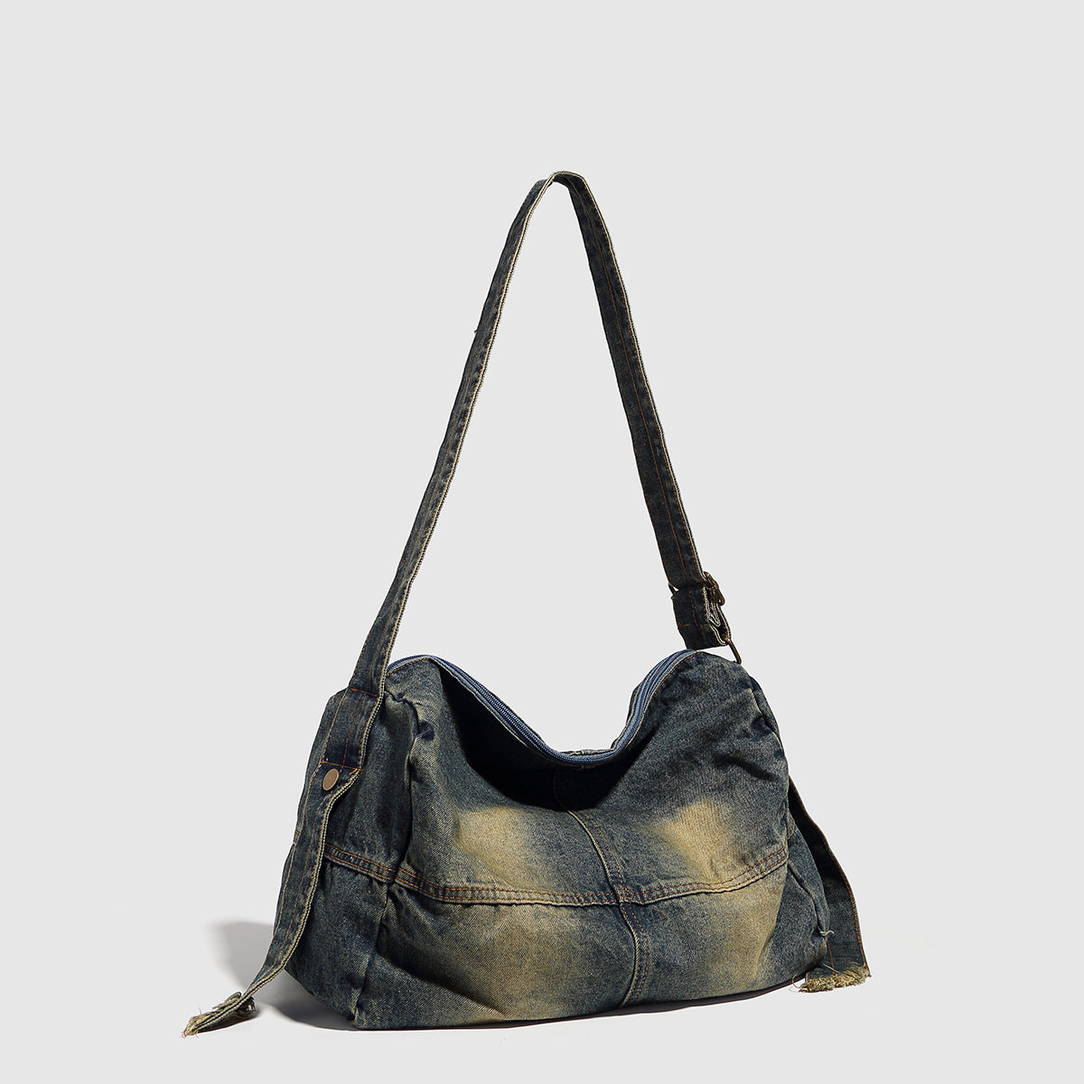Slouchy washed denim shoulder bag with faded distressed finish, zip-top closure, and antique brass-tone adjustable strap