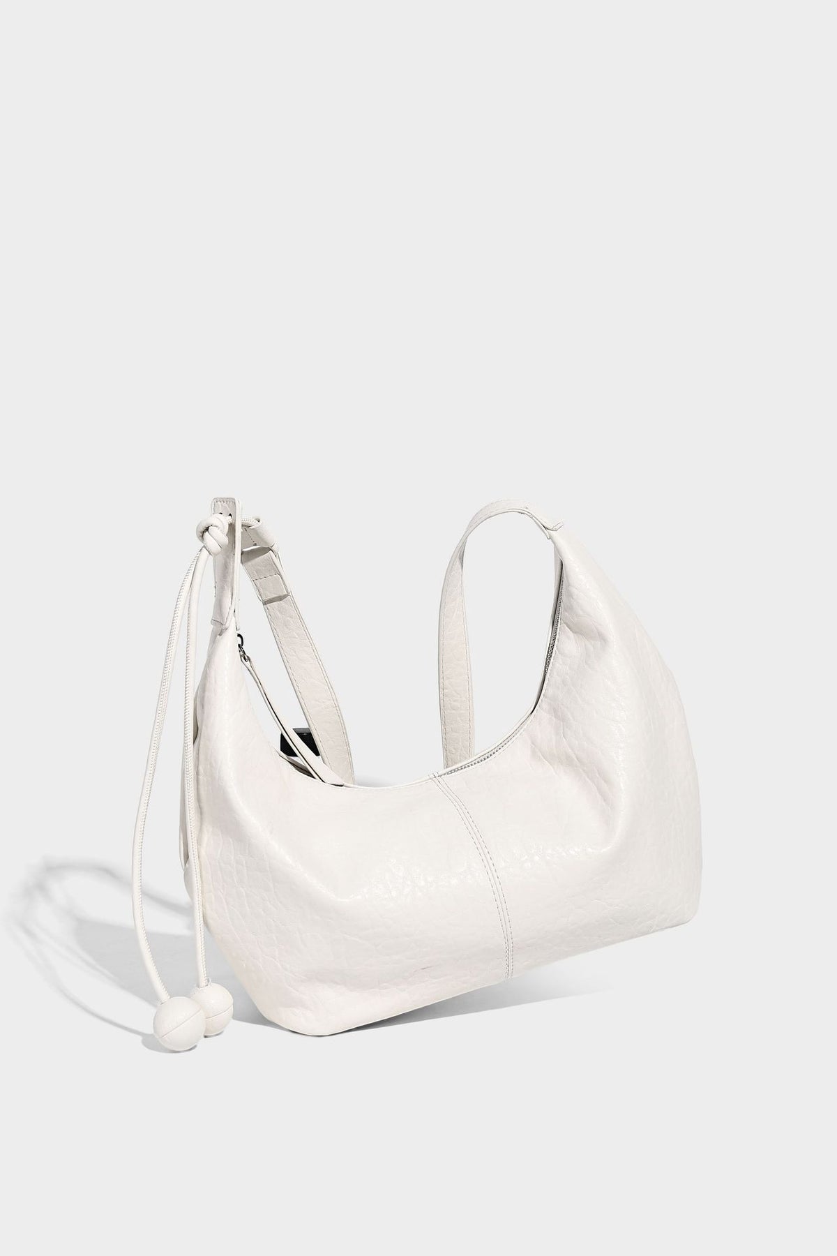 Slouchy crescent half-moon shoulder bag in pink pebbled textured finish with floral charm and knotted side detail, detail