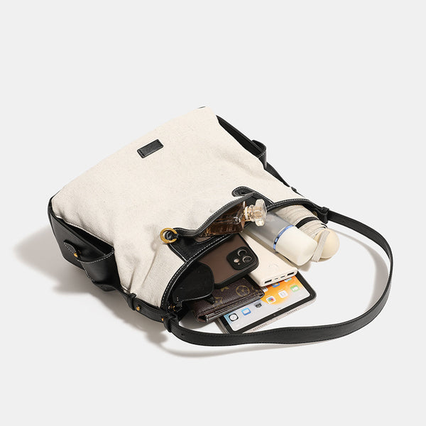 Off-white canvas hobo shoulder bag with black leather-look trim, gold-tone ring hardware, top zip closure, side pockets, and