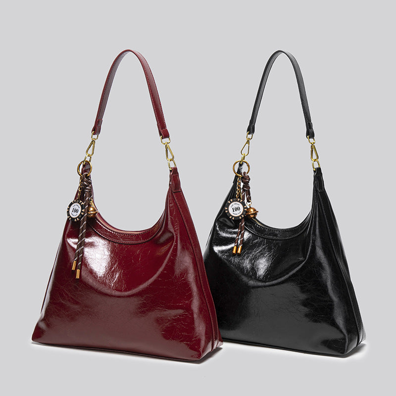 Große glänzende Hobo-Schultertasche in tiefem Burgunderrot mit Obermaterial in Lederoptik, Details in Goldoptik und dekorativem geflochtenem Anhänger, Detailansicht
