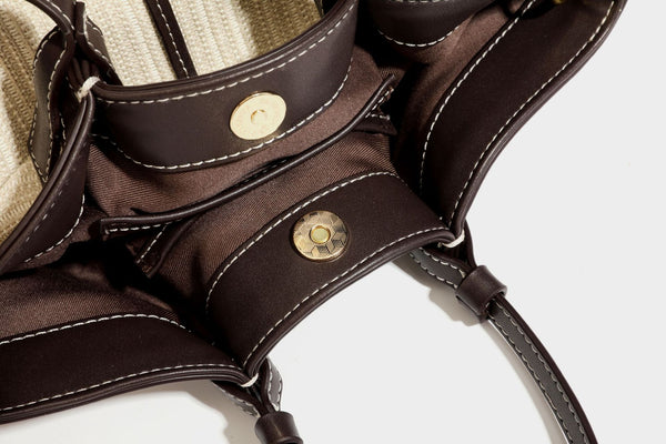 Cremefarbene geflochtene Tote-Bag mit dunkelbraunen Besätzen in Lederoptik, kontrastierenden weißen Nähten, zwei oberen Henkeln und abnehmbarem Schulter