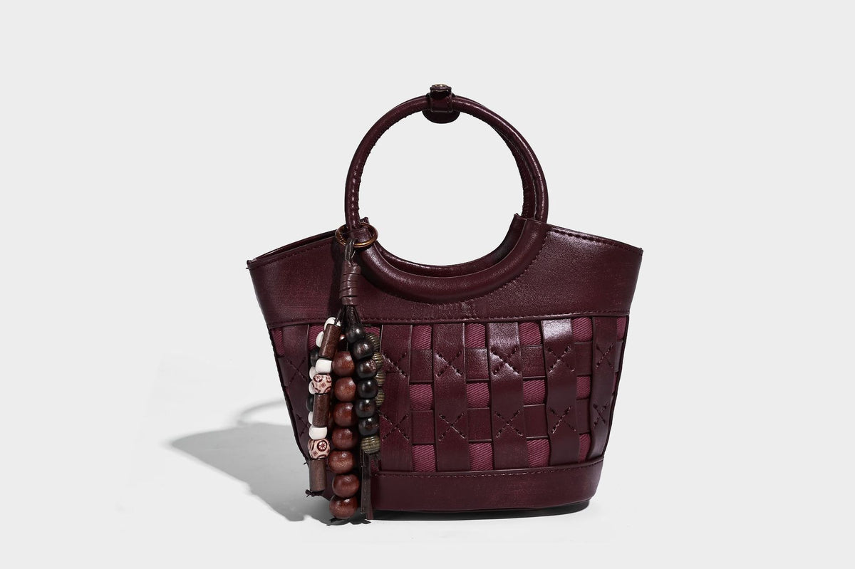 Small woven-panel bucket bag with circular ring handles, beaded tassel charm, and detachable crossbody strap in brown, detail