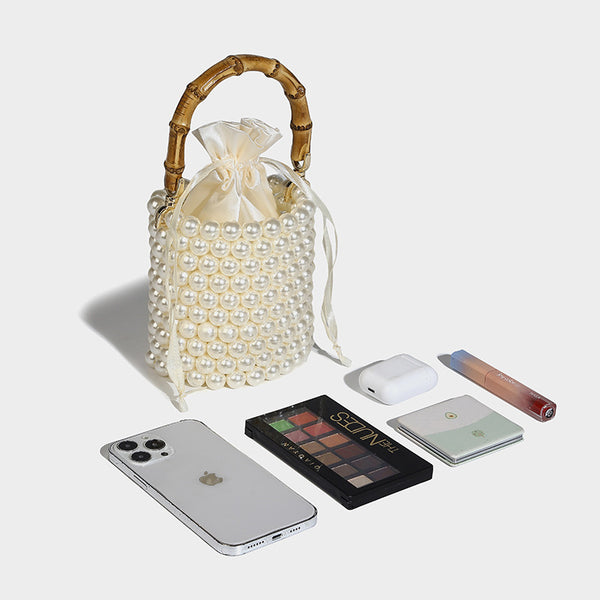 Small cylindrical bucket bag with glossy faux-pearl bead exterior, bamboo arched top handle, satin drawstring closure, and
