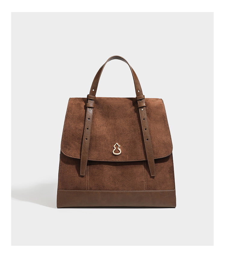 Structured suede-look convertible backpack handbag with flap closure and gold-tone emblem hardware in chocolate brown, detail