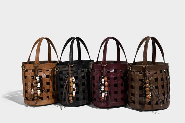 Small woven lattice bucket bag in brown leather-look finish with beaded tassel charm, dual top handles, and detachable