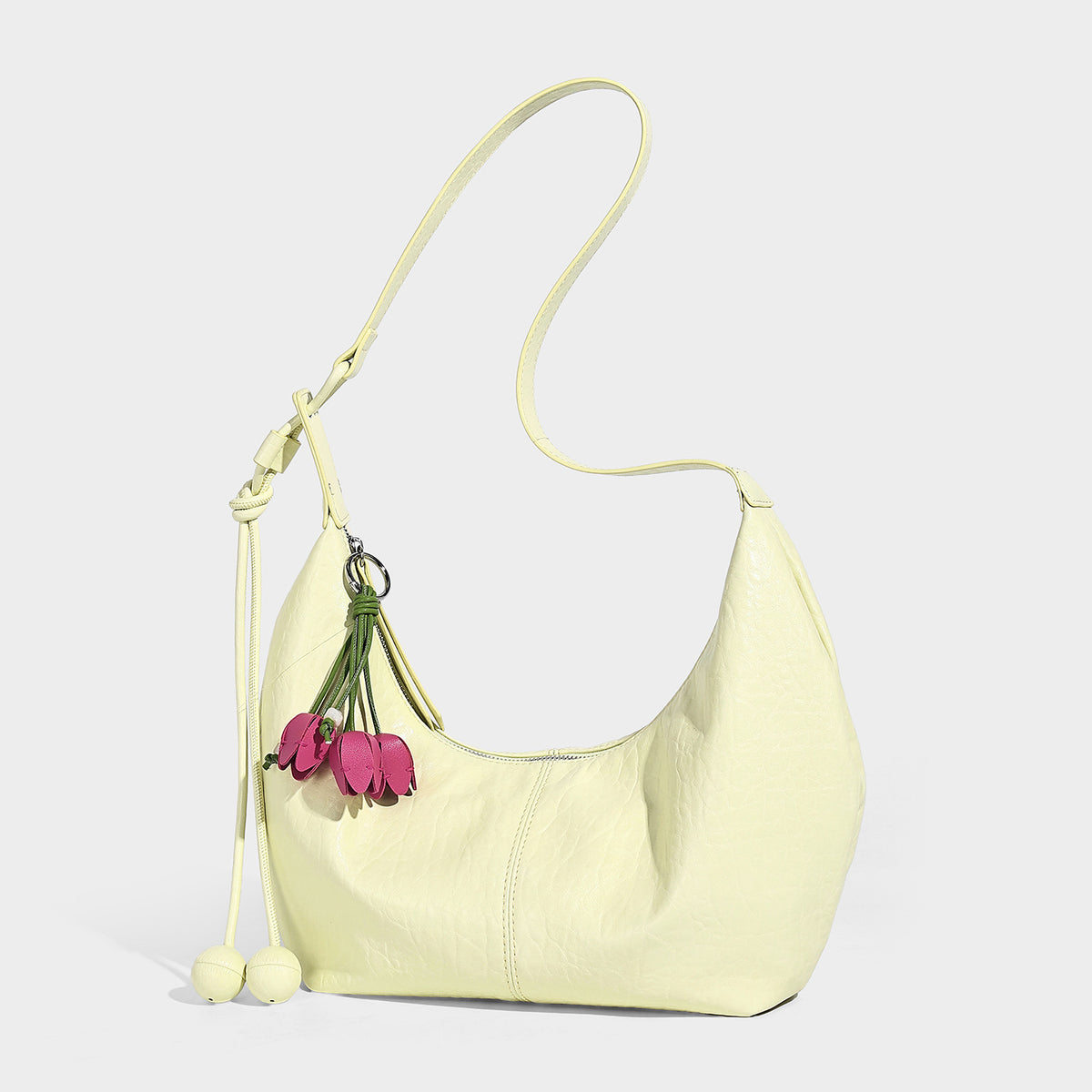 Slouchy crescent half-moon shoulder bag in pink pebbled textured finish with floral charm and knotted side detail, detail