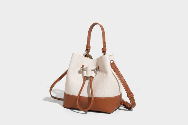 Small two-tone pebbled drawstring bucket bag with tan contrast base, metal toggle hardware, short top handle, and detachable