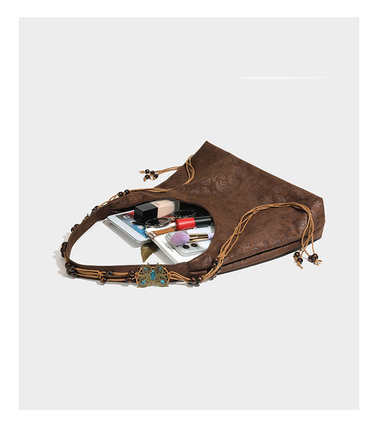 Slouchy boho hobo shoulder bag in embossed brown suede-look finish with beaded strap, cord tassels, and brass-tone leaf
