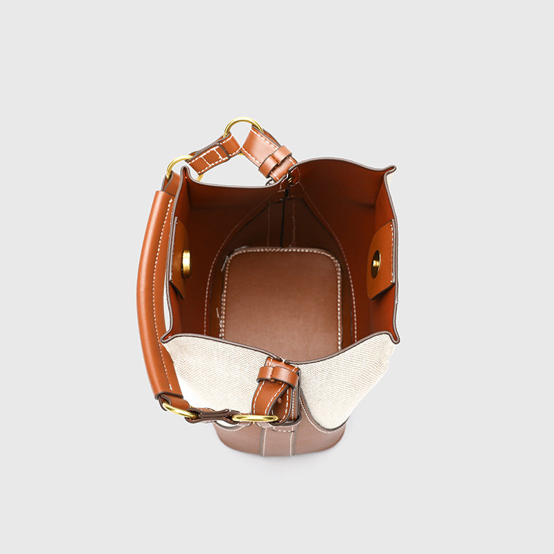 Cream canvas and tan leather-look bucket bag with arched top handle, wide detachable shoulder strap, and gold-tone hardware