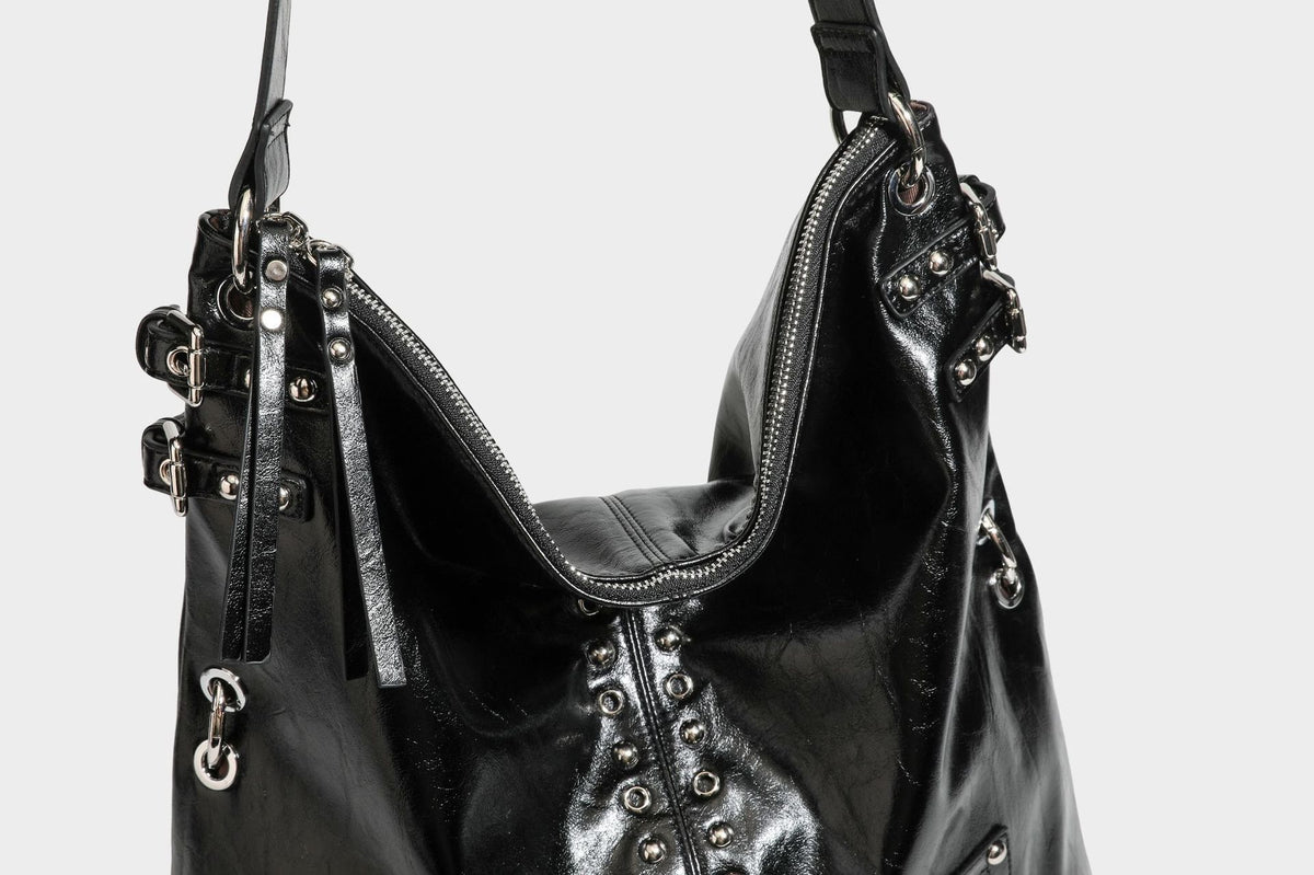 Black glossy leather-look slouchy shoulder bag with silver stud and eyelet hardware, top zip closure, front zip pocket, and