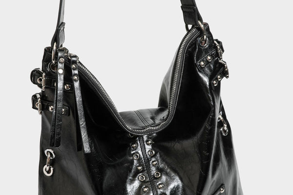 Black glossy leather-look slouchy shoulder bag with silver stud and eyelet hardware, top zip closure, front zip pocket, and