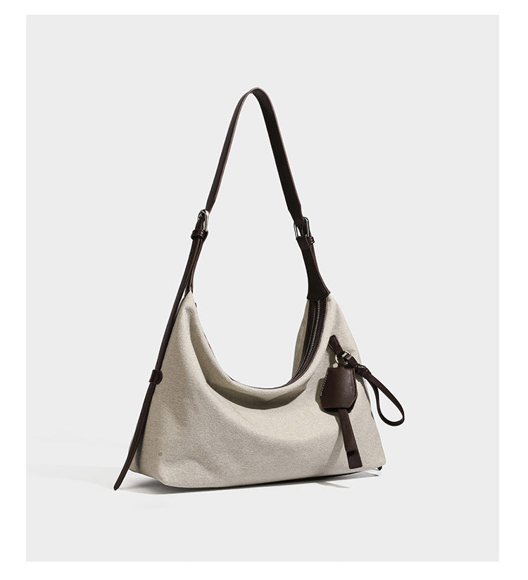Lässig geschnittene Hobo-Schultertasche aus Canvas in Haferflockenfarbe mit dunkelbraunem Besatz in Lederoptik, silberfarbenem Reißverschluss und langem, verstellbarem