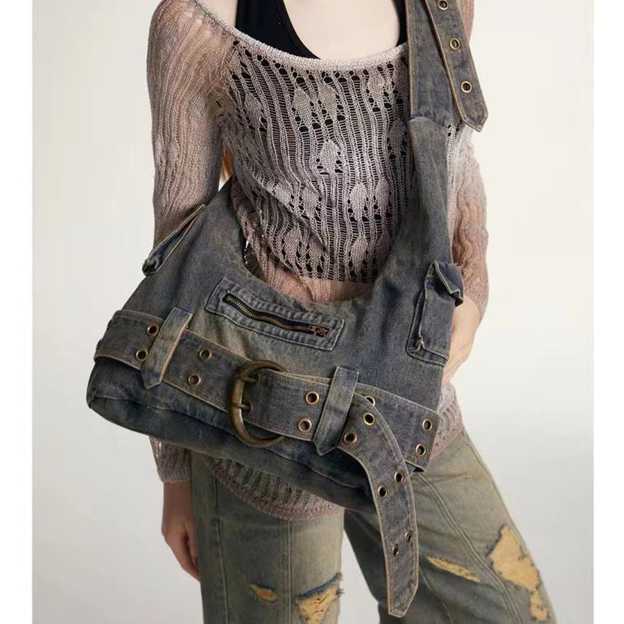 Washed blue-gray denim slouchy hobo shoulder bag with wide grommeted belt panel, brass-tone D-ring buckle, exterior zip