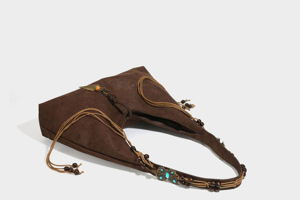 Slouchy boho hobo shoulder bag in embossed brown suede-look finish with beaded strap, cord tassels, and brass-tone leaf