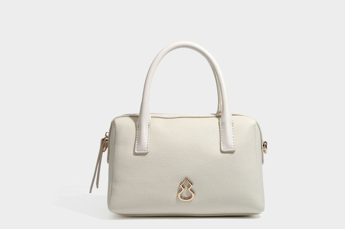 Small structured pillow satchel bag with pebbled leather-look finish, dual rolled top handles, gold-tone gourd emblem, and