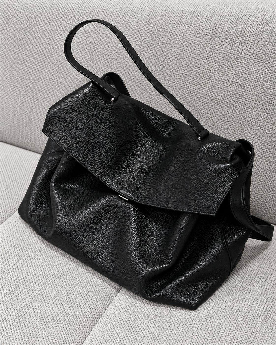 Large black slouchy leather-look shoulder bag with V-shaped envelope flap, silver-tone clasp, and adjustable strap, detail