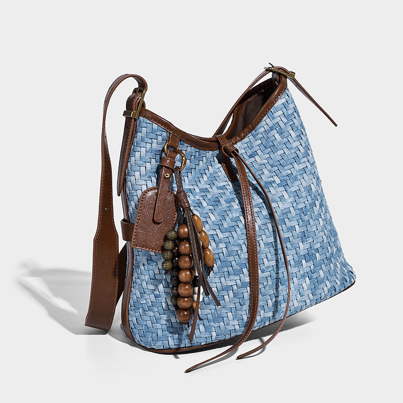 Light blue woven bucket bag with brown leather-look trim, gold-tone hardware, adjustable shoulder strap, and decorative bead