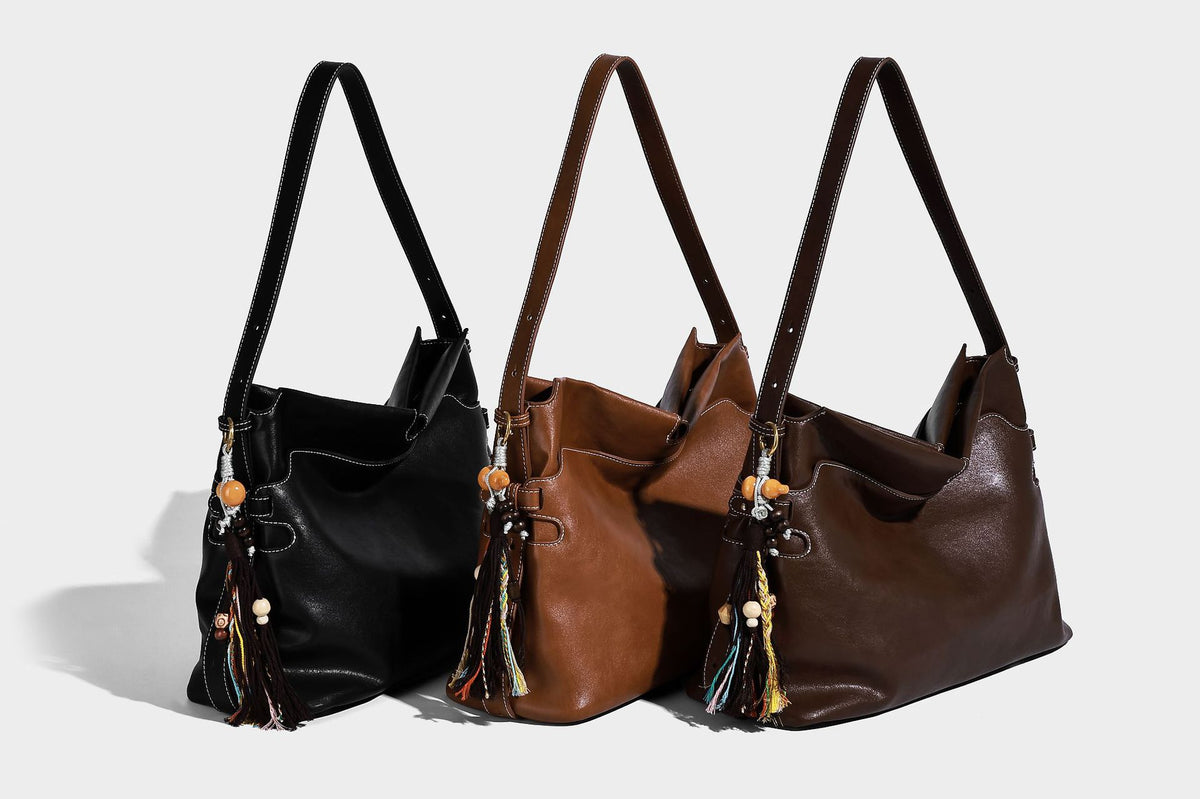 Large slouchy leather-look hobo tote bag with open top, adjustable shoulder strap, and colorful tassel bead charm, detail