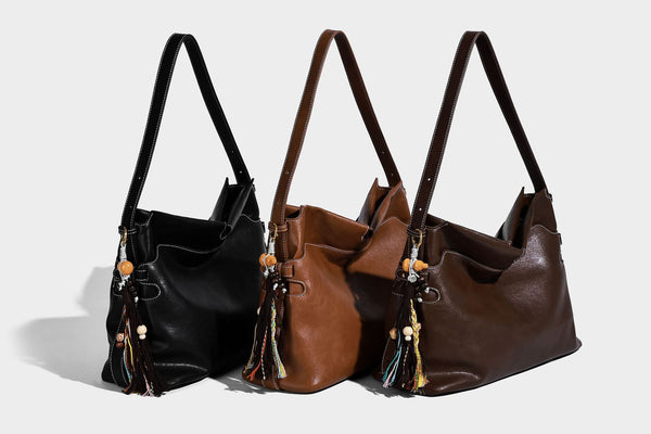 Large slouchy leather-look hobo tote bag with open top, adjustable shoulder strap, and colorful tassel bead charm, detail