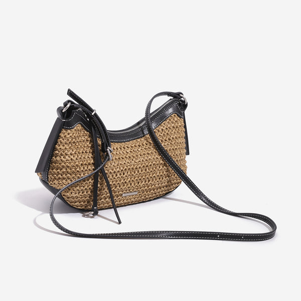 Tan woven straw half-moon shoulder bag with black leather-look trim, zip closure, tassel pull, and adjustable crossbody