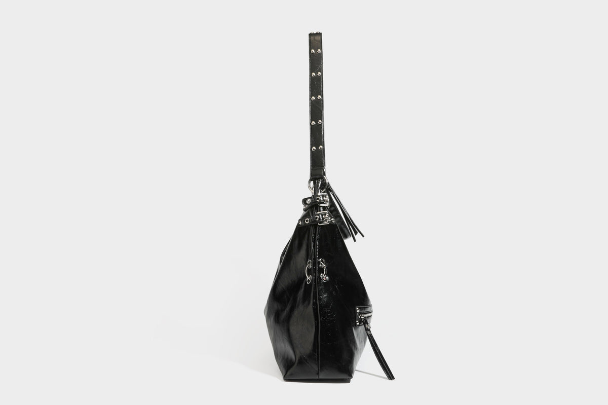 Black glossy leather-look slouchy shoulder bag with silver stud and eyelet hardware, top zip closure, front zip pocket, and