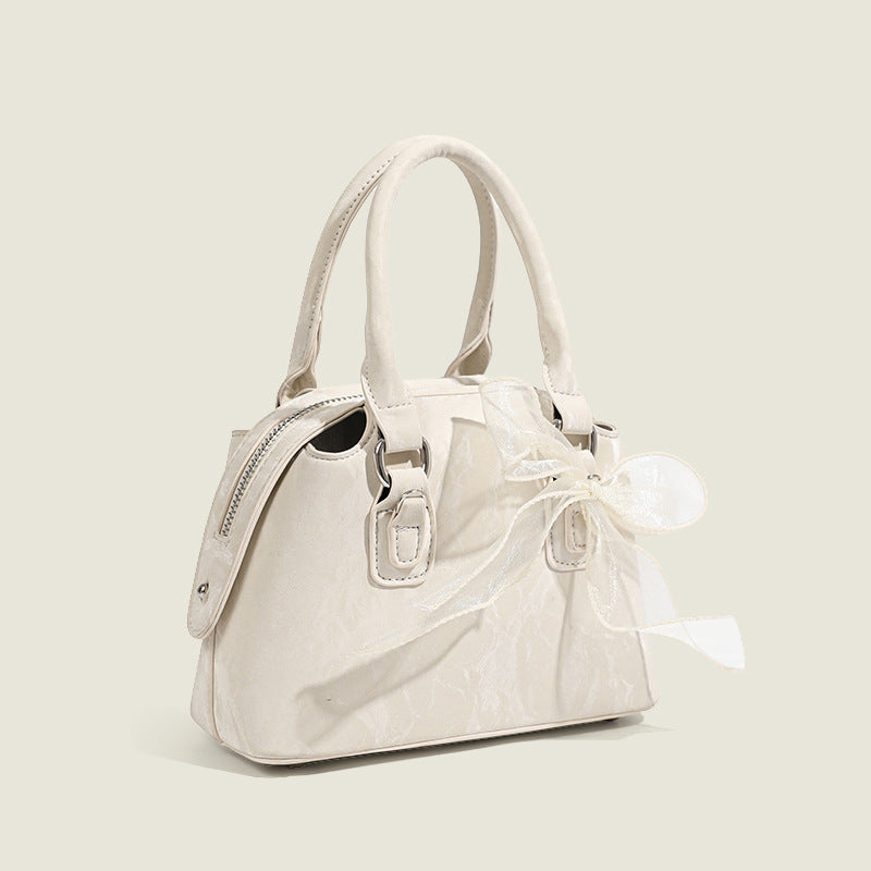 Small structured Boston bag in cream with glossy crinkled finish, sheer bow accent, silver-tone hardware, dual top handles