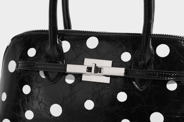 Glossy structured polka-dot satchel bag with dual top handles, silver turn-lock hardware, and detachable shoulder strap