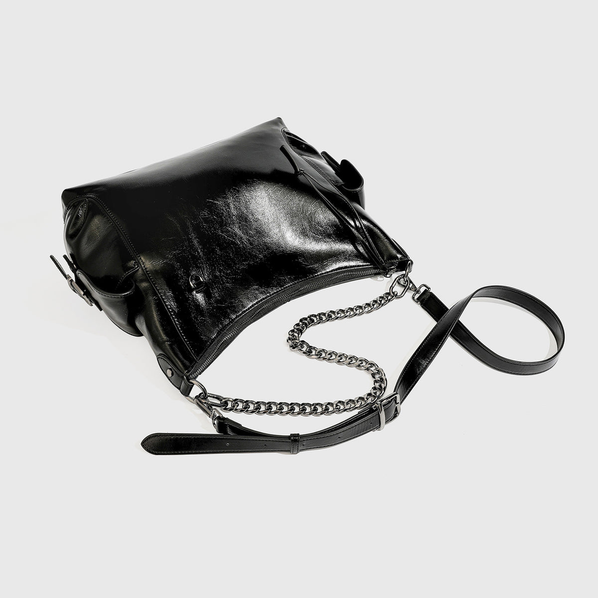 Slouchy hobo shoulder bag with glossy leather-look finish, silver-tone chain drape across front, side buckle pockets, and