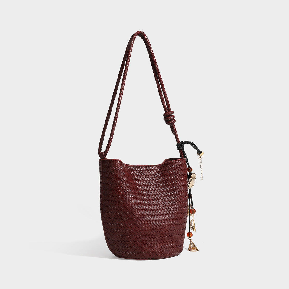 Olive green woven leather-look bucket bag with braided crossbody strap, knotted adjustment, and gold-tone tassel charm with