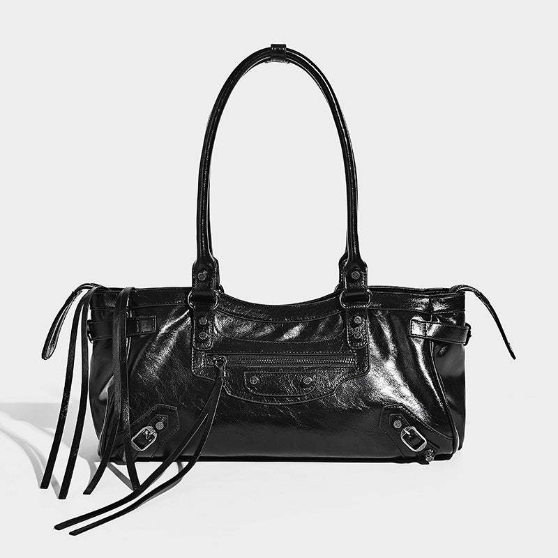 Elongated barrel shoulder bag with glossy leather-look finish, silver stud hardware, side tassels, and multiple exterior zip