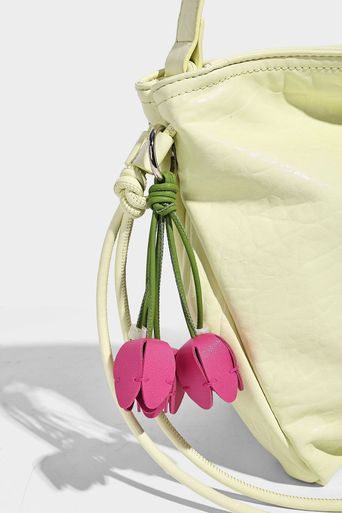 Slouchy hobo shoulder bag in pale yellow with slim strap, drawstring bead closure, and pink tulip floral charm, detail view