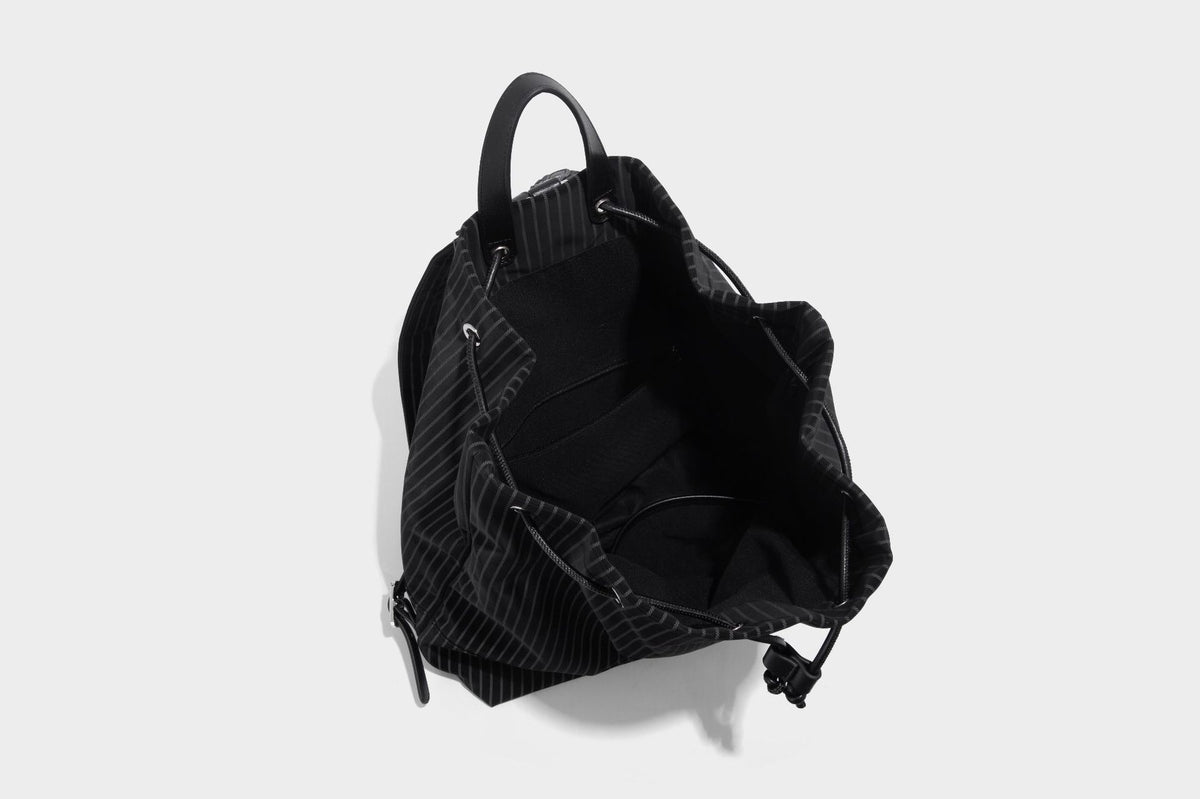 Schwarze wandelbare Rucksack-Handtasche mit Nadelstreifen, Kordelzugverschluss, Tragegriff aus Lederimitat und matten Metallbeschlägen, Detailansicht