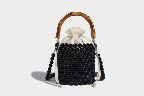 Small cylindrical bucket bag with glossy faux-pearl bead exterior, bamboo arched top handle, satin drawstring closure, and