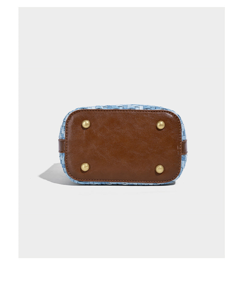 Small light blue woven bucket bag with brown leather-look trim, braided top handle, brass-tone ring hardware, drawstring