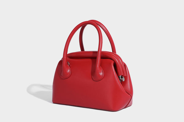 Small structured shell top-handle bag in red with heart charm and braided cord detail, smooth leather-look finish, detail
