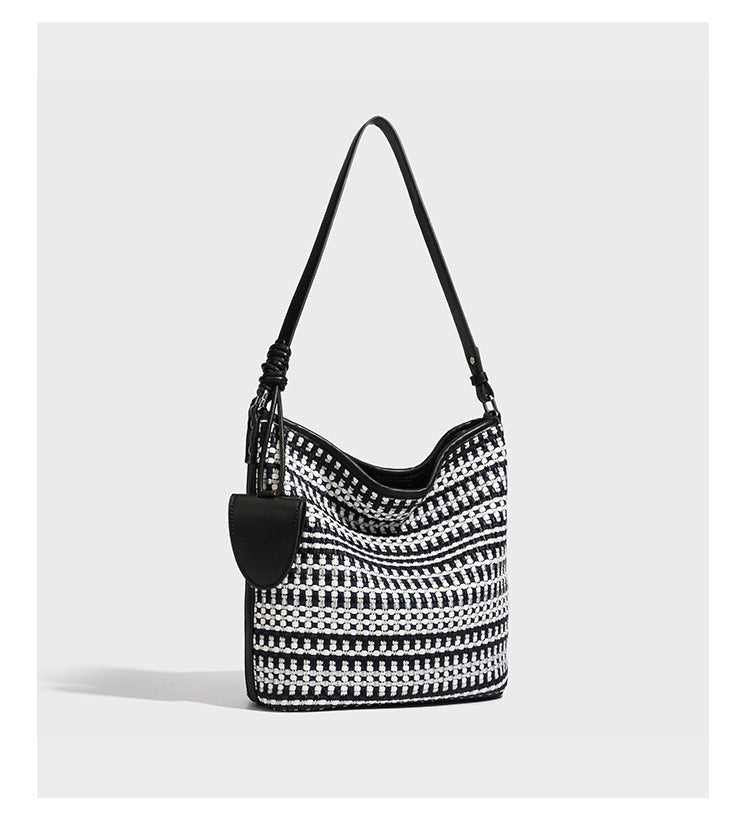 Woven stripe bucket shoulder bag in cream and dark brown with leather-look trim, knotted adjustable strap, and small shield